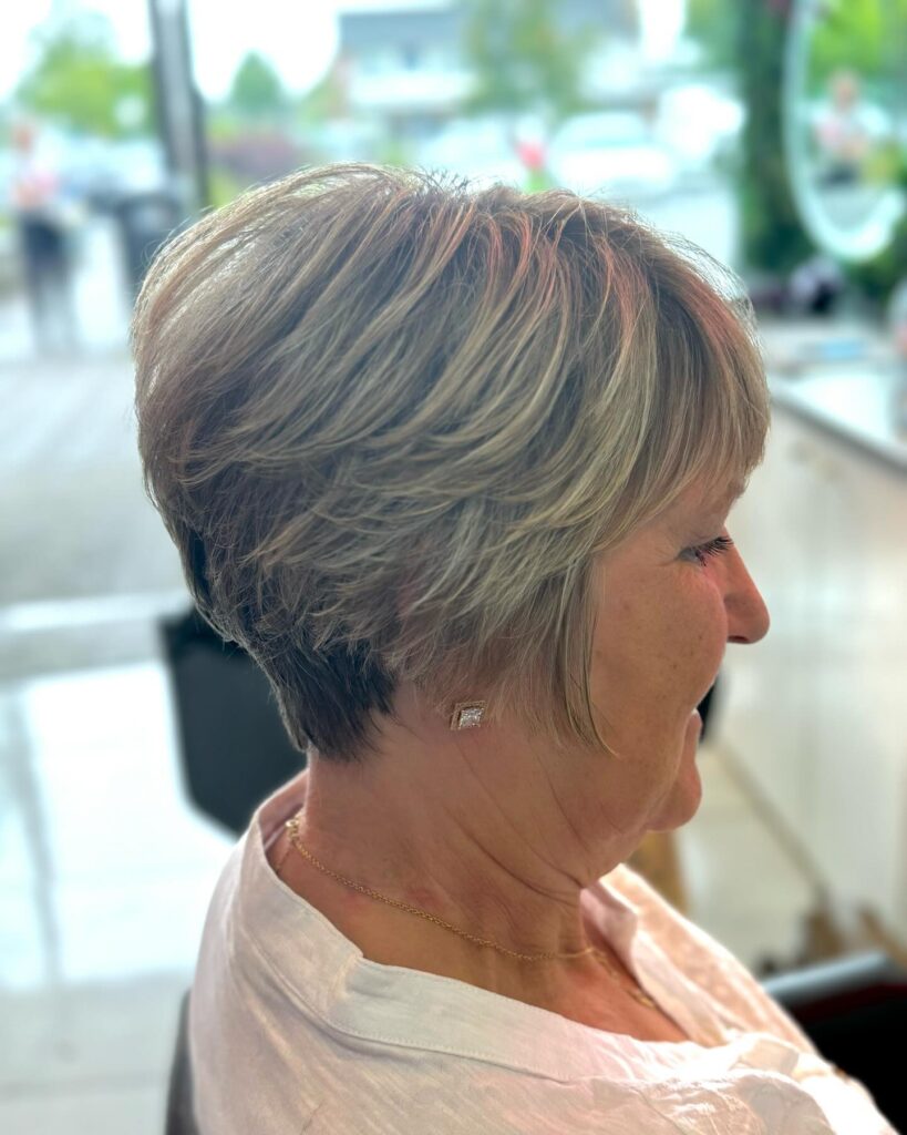 A side profile of a woman wearing a layered ash blonde bixie cut with a stacked back and feathered texture.