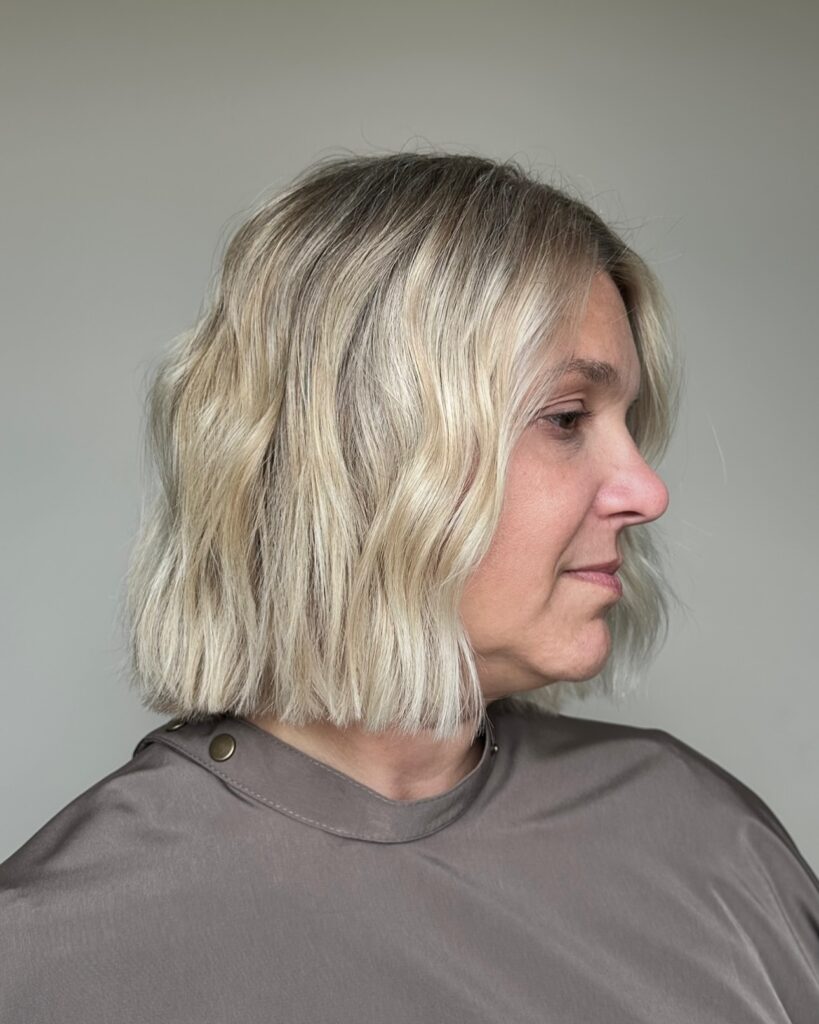 A woman with a shoulder-length ash-blonde blunt bob styled in soft beachy waves.