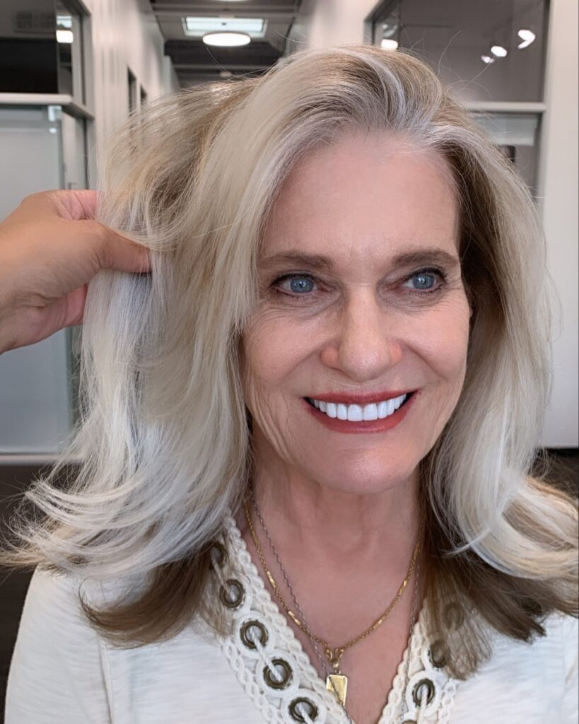 A smiling woman with medium-length platinum blonde hair featuring flipped ends and voluminous layers.