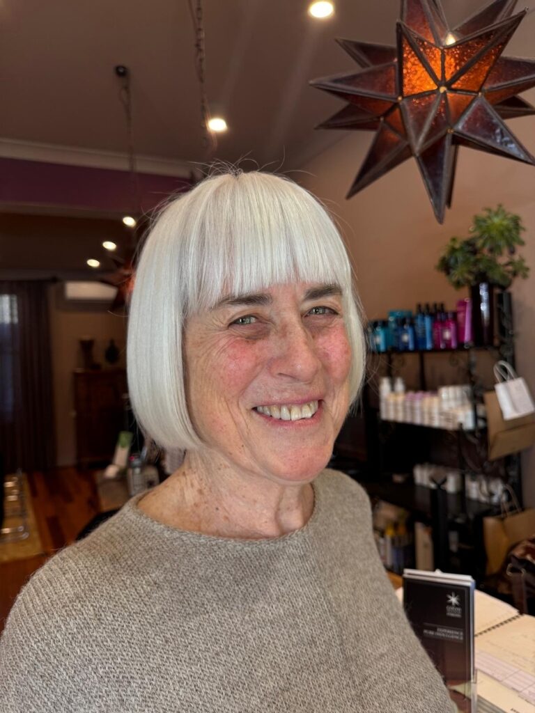 A woman with a chin-length, sleek, silver bob and straight-across blunt bangs.