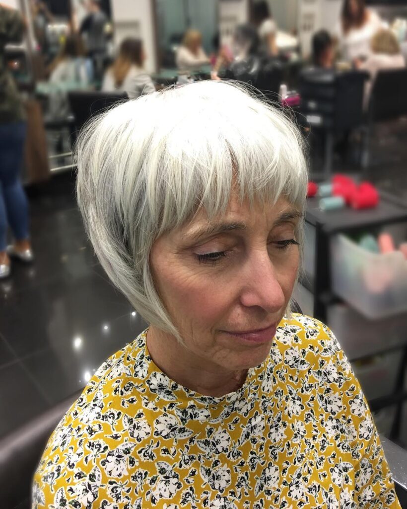 A woman with a short, tapered silver pixie cut featuring wispy bangs and piecey layers.