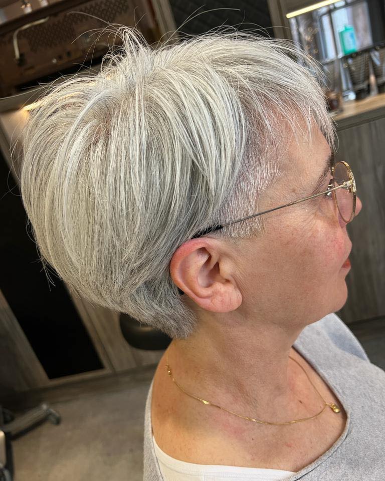 A woman in profile wearing a short silver and grey pixie cut with buzzed sides and a textured voluminous top.
