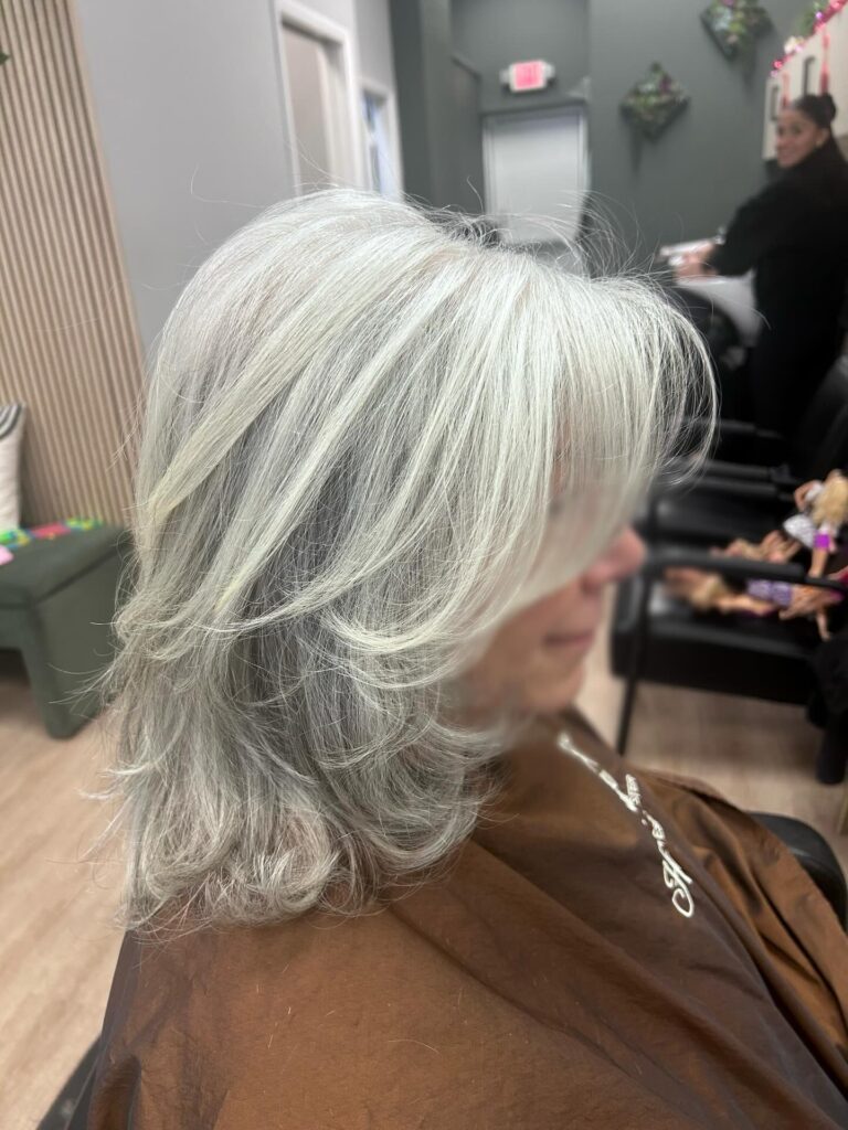 A woman with shoulder-length feathered silver hair featuring long layers and side-swept bangs.
