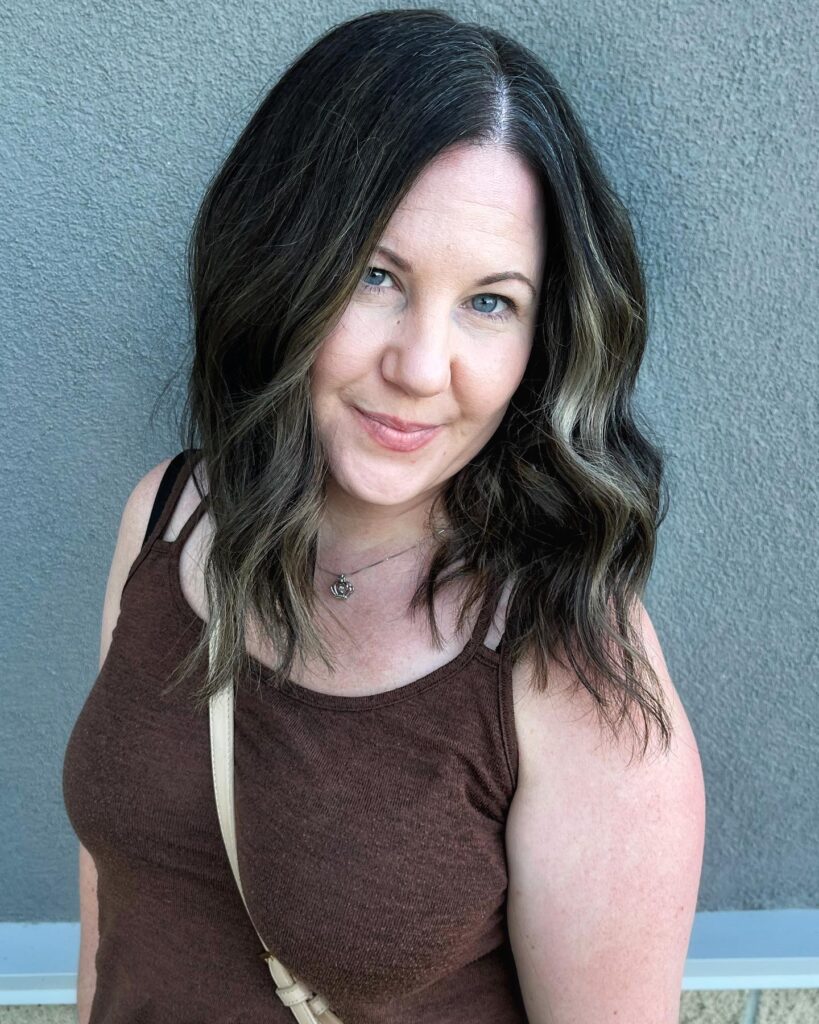 A woman with shoulder-length dark brunette hair featuring caramel balayage and loose beachy waves.