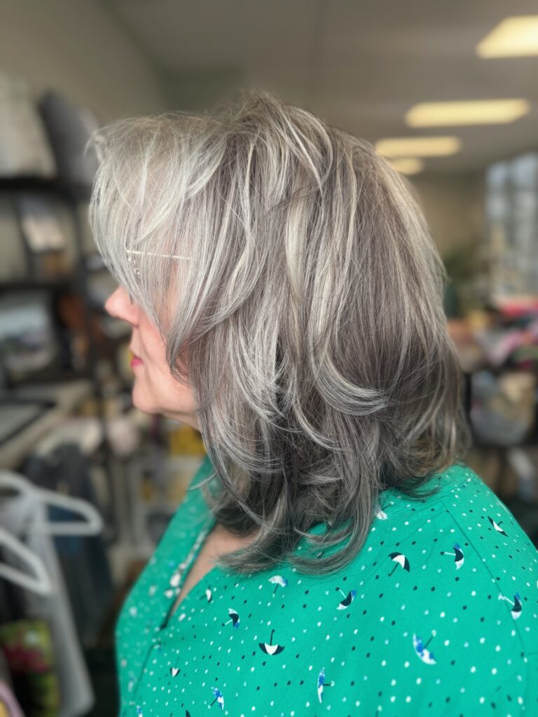 A woman in profile with a shoulder-length silver shaggy haircut featuring voluminous feathered layers and wispy bangs.