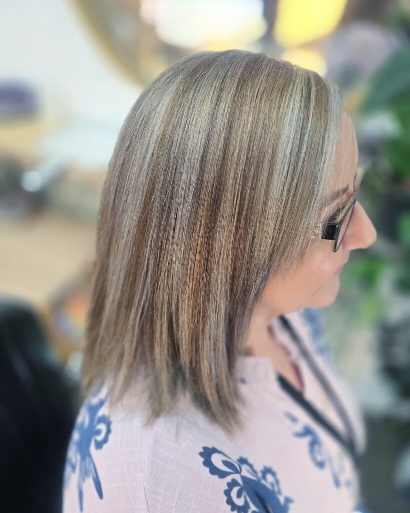 A side profile of a woman with straight shoulder-length sandy blonde hair featuring light highlights and long blended bangs.