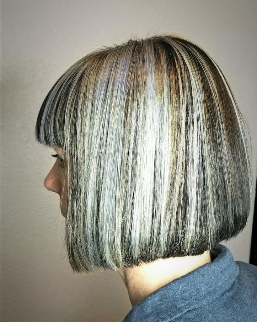 A side profile of a woman with a blunt chin-length bob featuring high-contrast silver and blonde highlights and a straight-across fringe.
