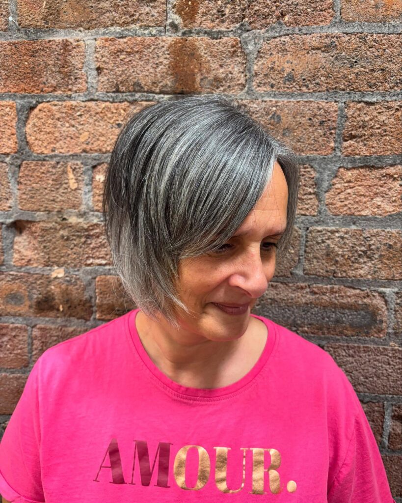 A woman with a chin-length salt and pepper bob featuring a side-swept fringe and straight texture.