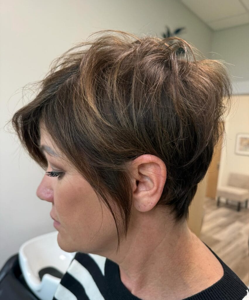 Brunette layered pixie haircut with tapered nape and wispy side pieces.