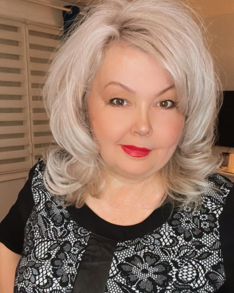 A woman with bright platinum blonde shoulder-length hair styled with lots of volume and side-swept bangs.