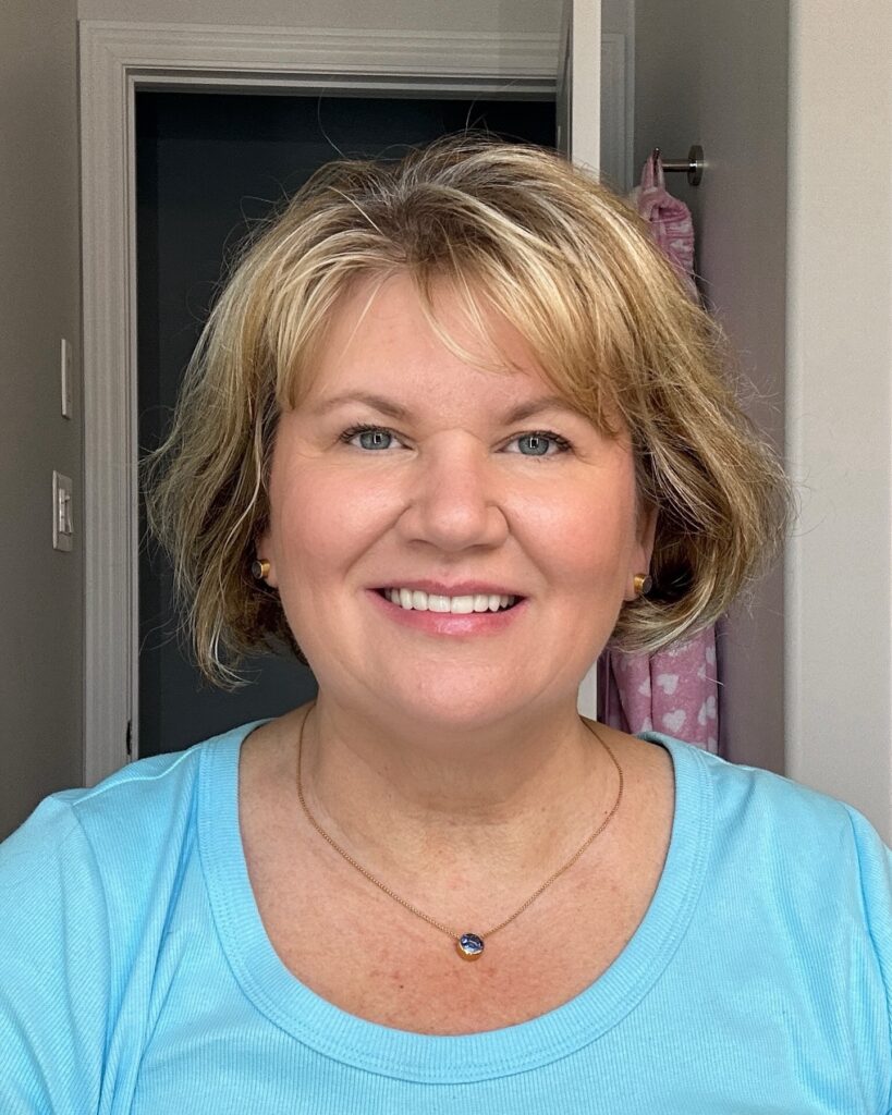 A smiling woman with a chin-length golden blonde bob and piecey, textured bangs.