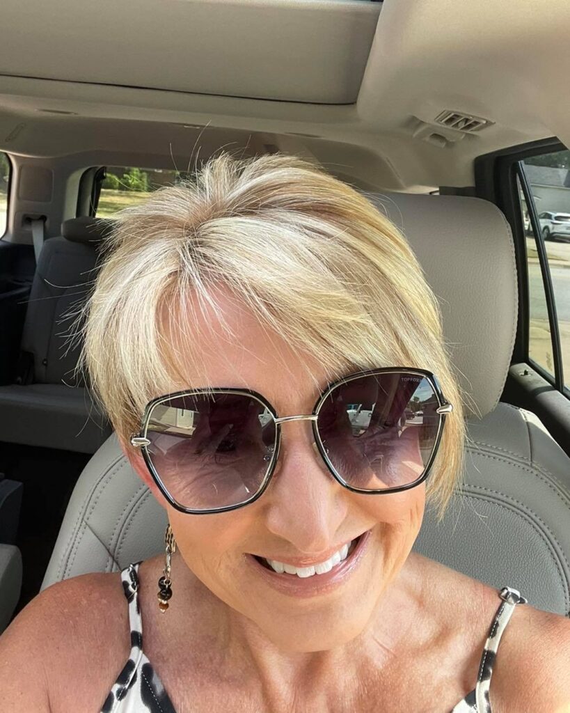 A woman wearing sunglasses with a short, champagne-blonde pixie cut and wispy bangs.