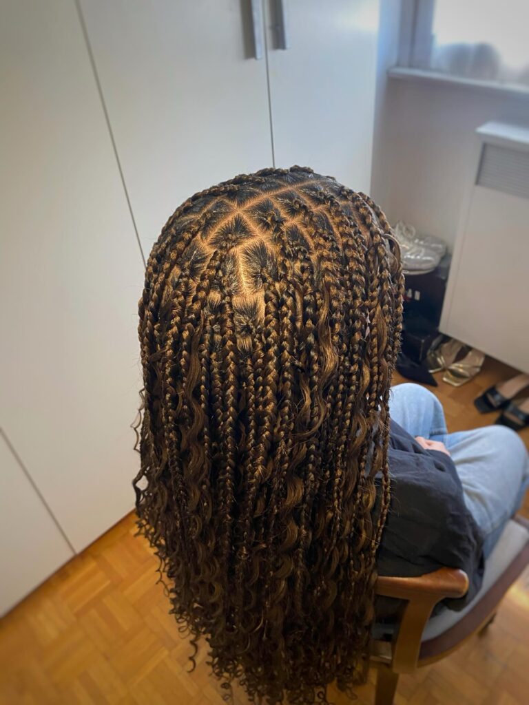 Long caramel brown goddess braids with curly ends and detailed square parting.