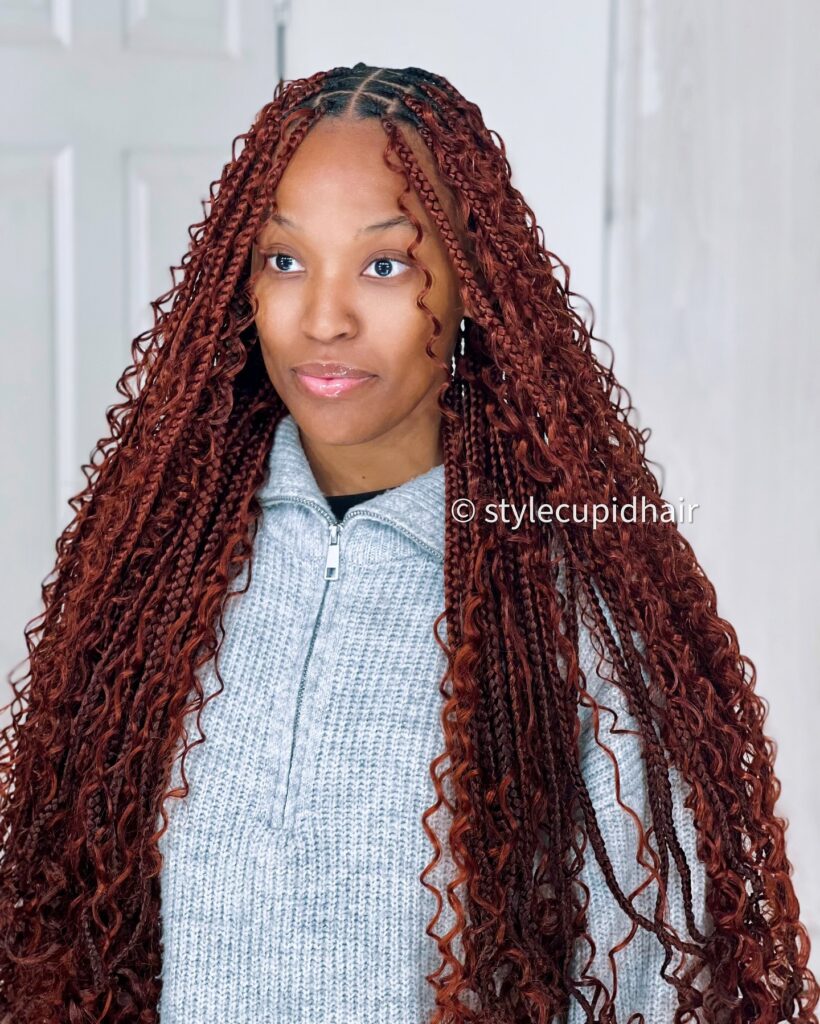 Copper red goddess braids with long curly strands and center parted braids framing the face.
