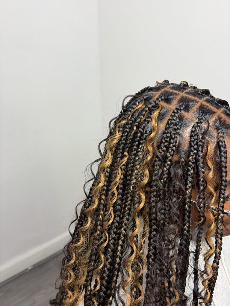 Black goddess braids with golden blonde curly highlights and neat square parts styled in medium length braids.