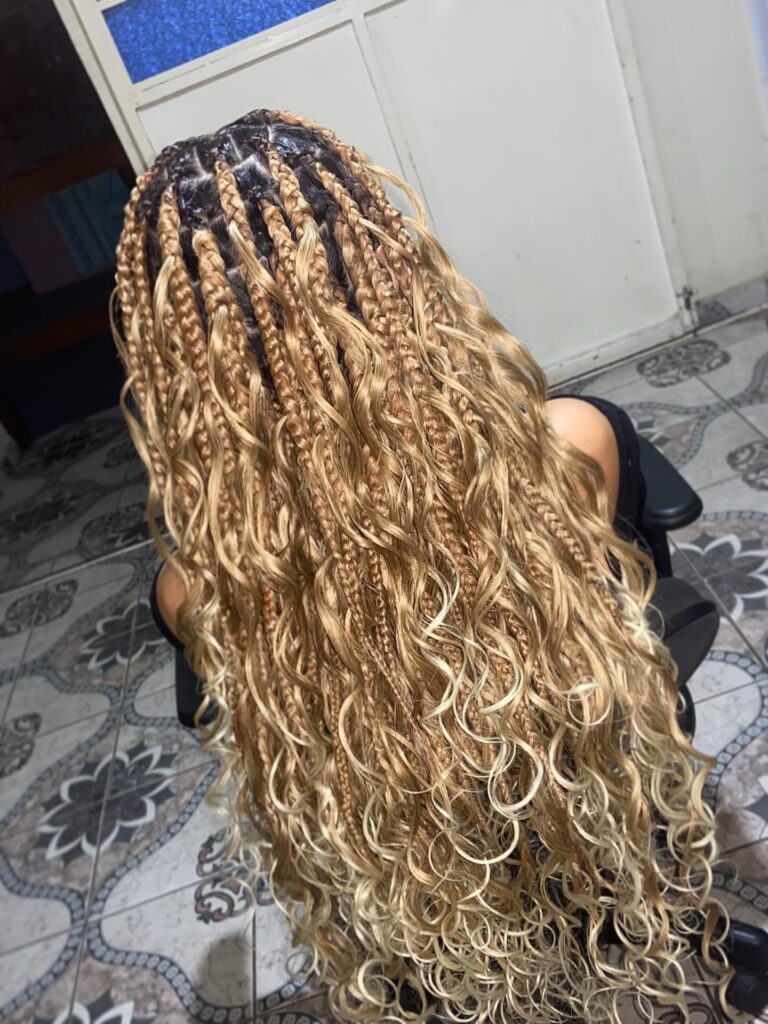 Long sandy blonde goddess braids with loose curly ends and blended blonde highlights throughout.