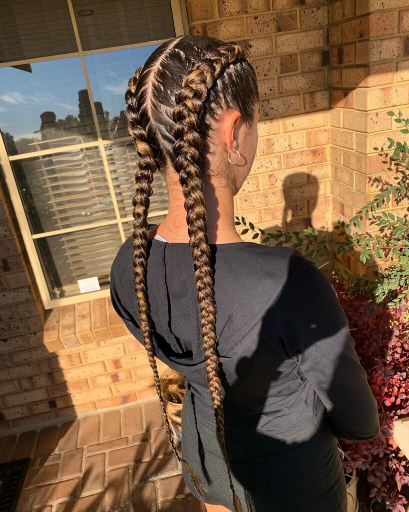 Long sleek Dutch braids with dark brown and caramel tones styled in clean center parted sections.