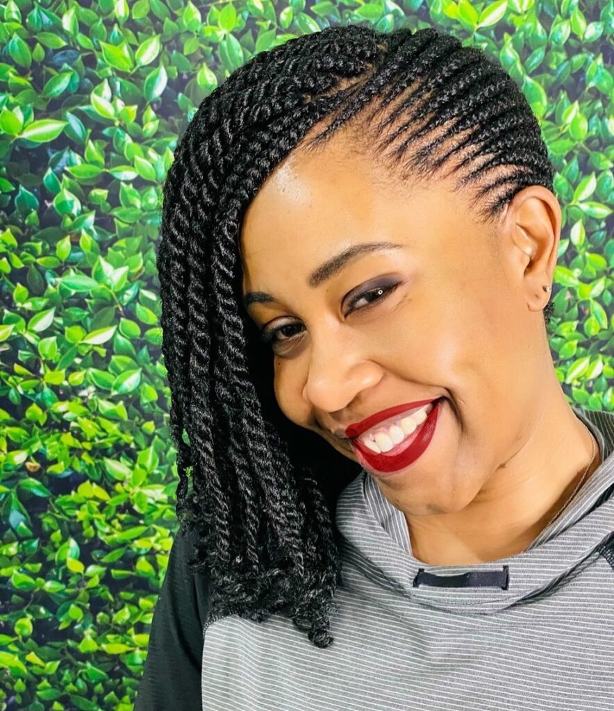 A woman smiling with a side-swept black passion twist bob featuring neat side cornrows.
