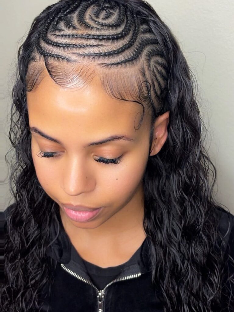 A woman showing off intricate swirled cornrow patterns on top with long, loose, wavy black hair.