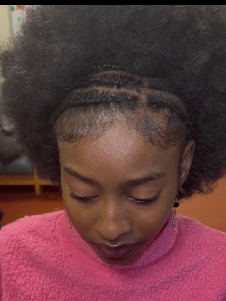 A young woman with a large natural afro and thin horizontal cornrows braided across the front of her hairline.