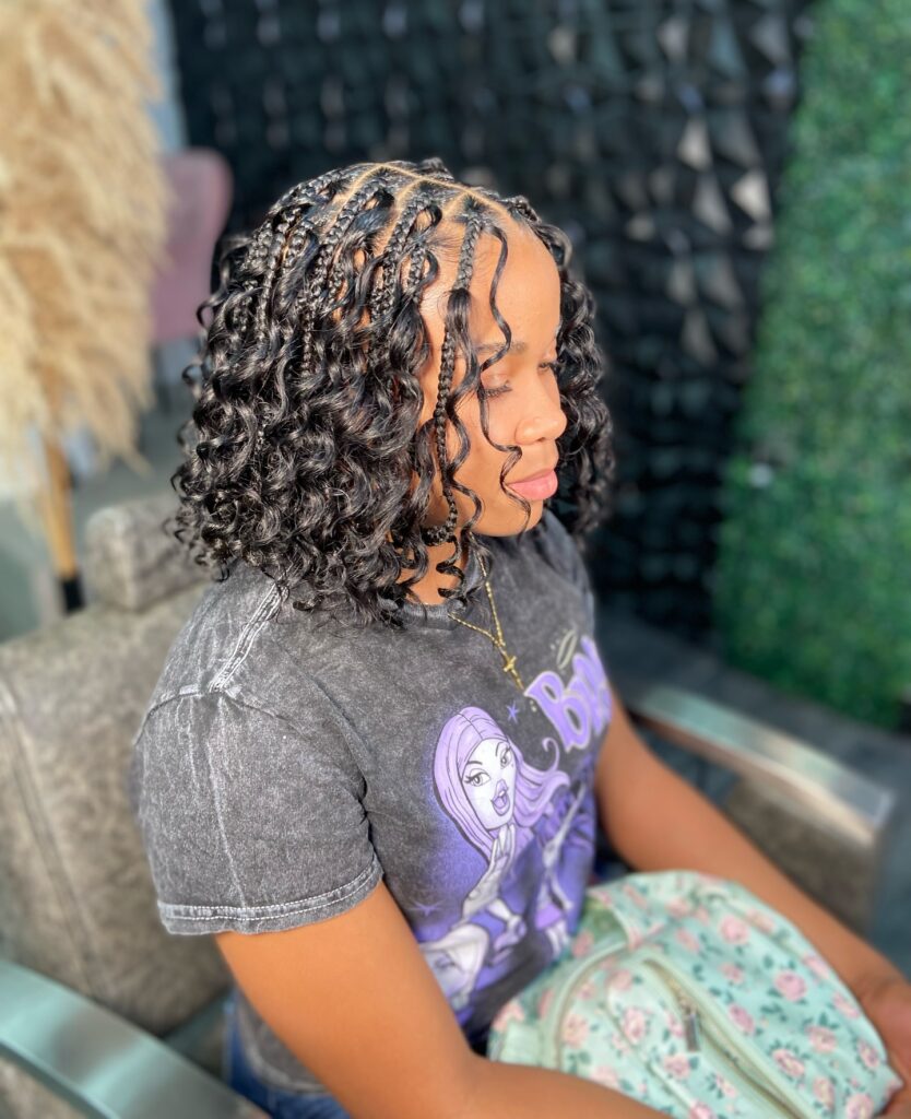 A woman with shoulder-length black braids that end in tight shiny curls styled a bob.