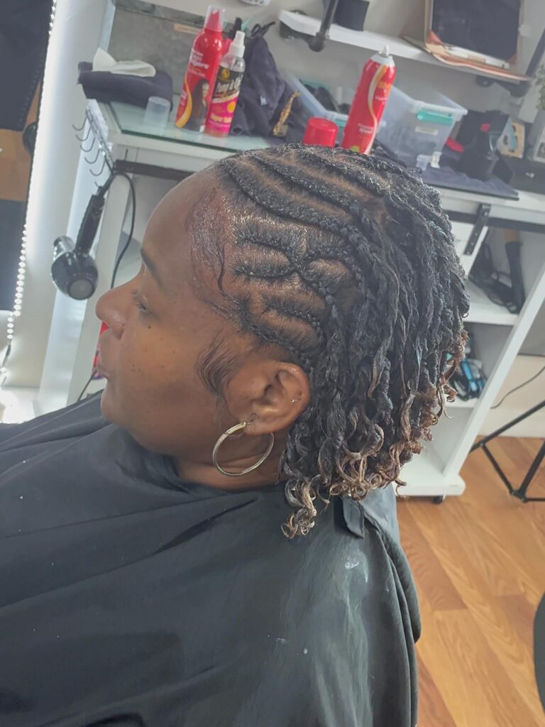 A woman with a short braided bob featuring neat cornrows and black twists with light brown curly ends.