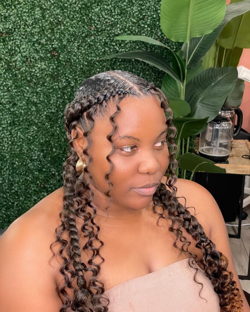 A woman wearing long boho braids with honey brown highlights and loose spiral curls framing her face.