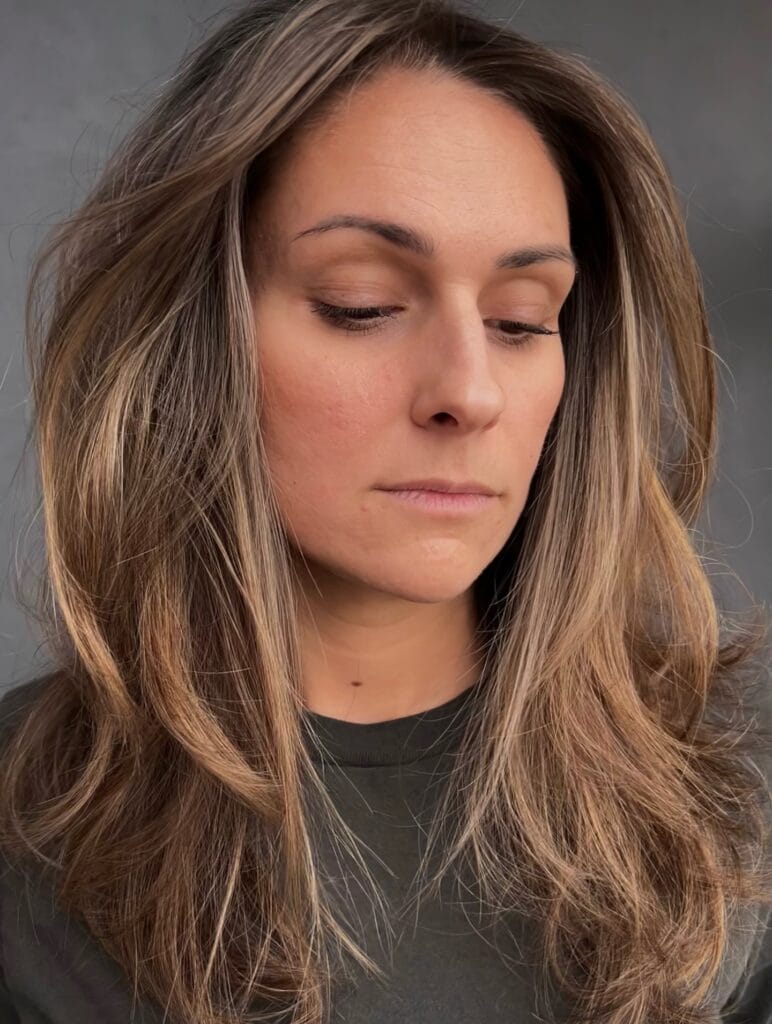 Long brunette hair with soft layers and subtle face framing highlights.