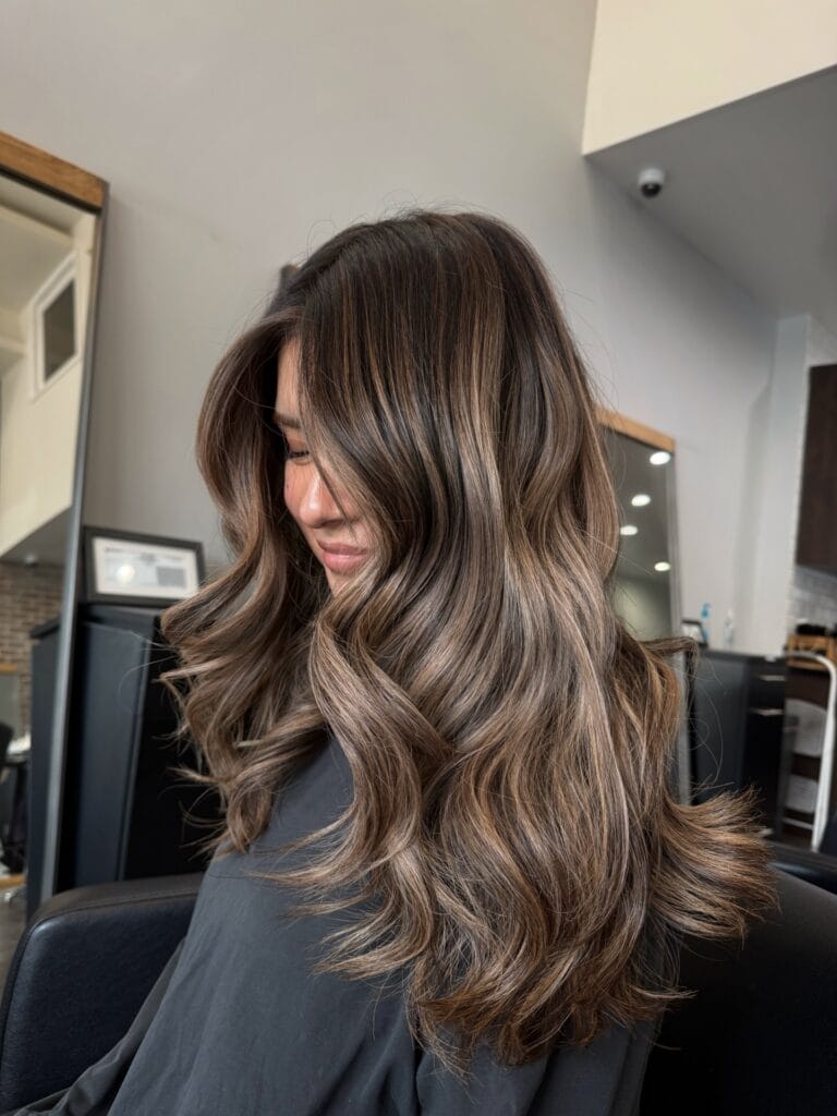 Long layered brunette hair with soft waves and face framing highlights.