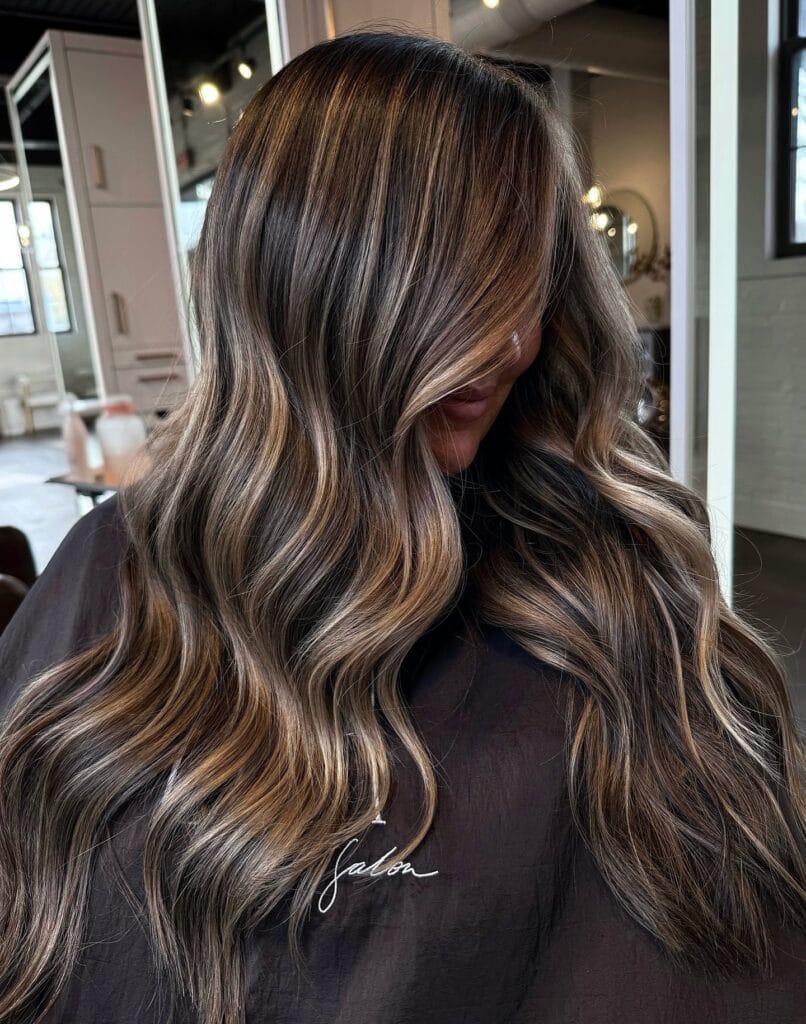 Long brunette hair with soft waves and honey highlights framing the face.