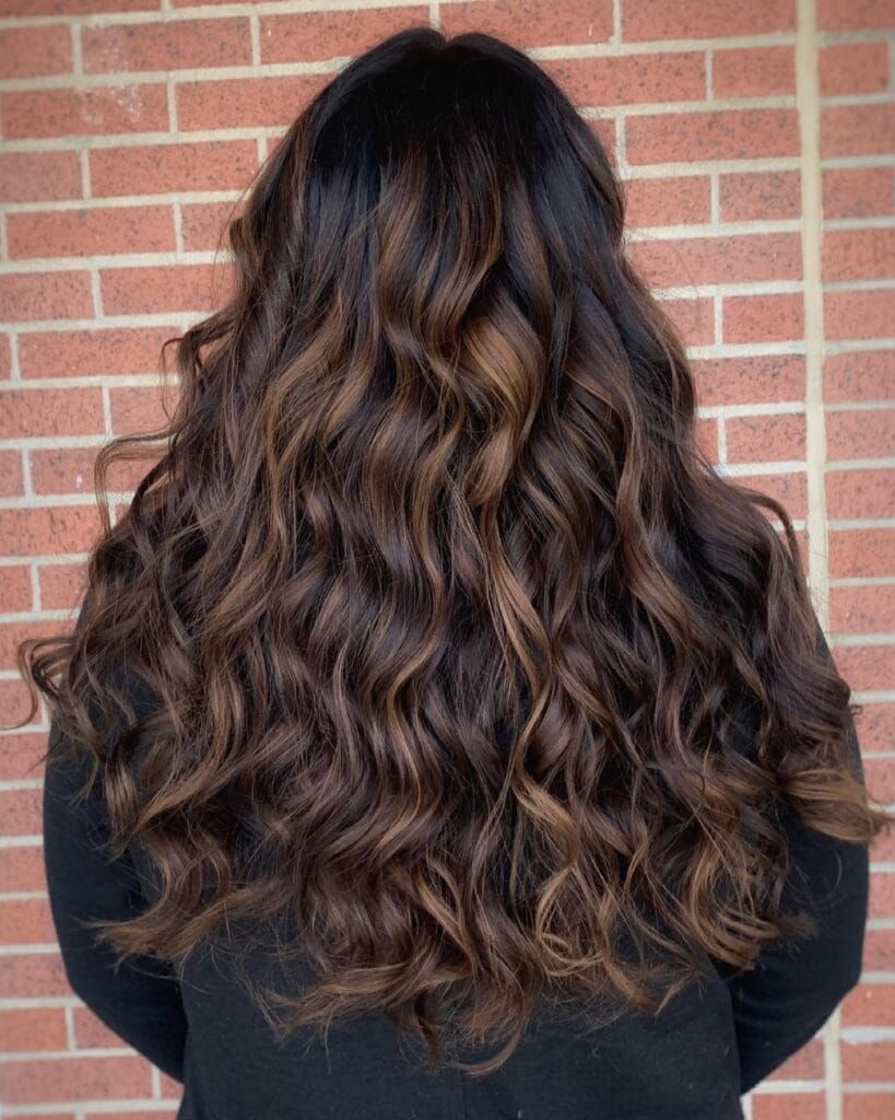 Long wavy brunette hair with warm caramel highlights and soft defined texture.