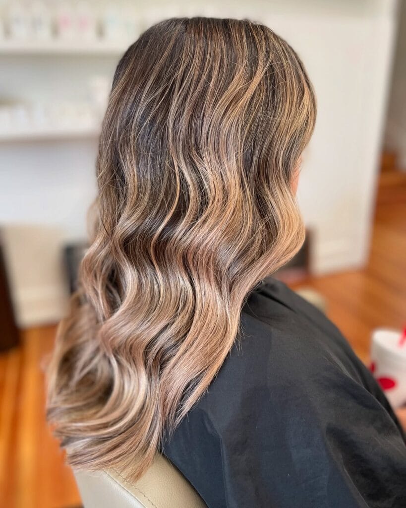 Long brunette hair with soft waves and a sandy blonde color melt toward the ends.