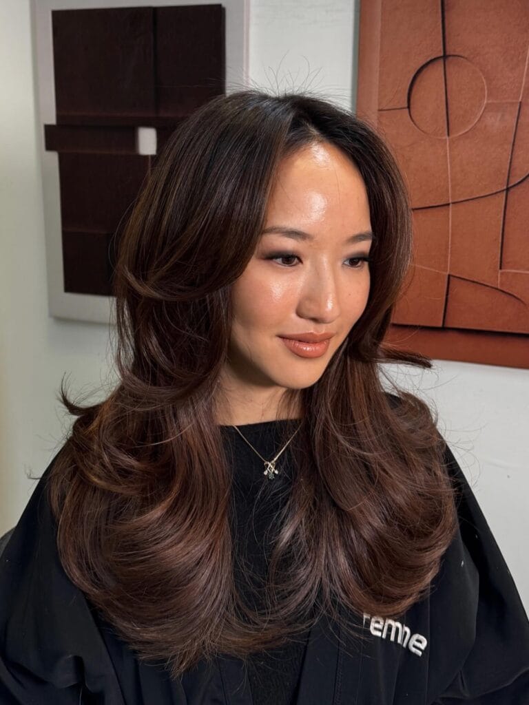 Long brunette hair with a voluminous blowout and warm caramel highlights.