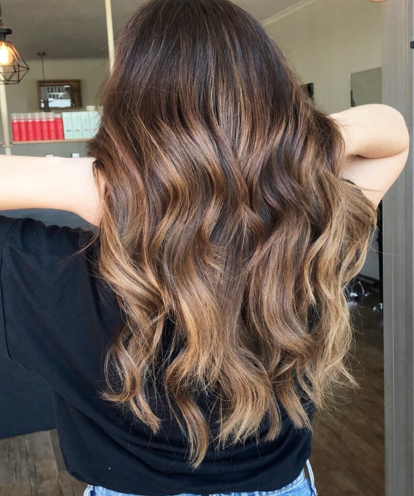 Long wavy brunette hair with warm caramel highlights and soft beachy texture.