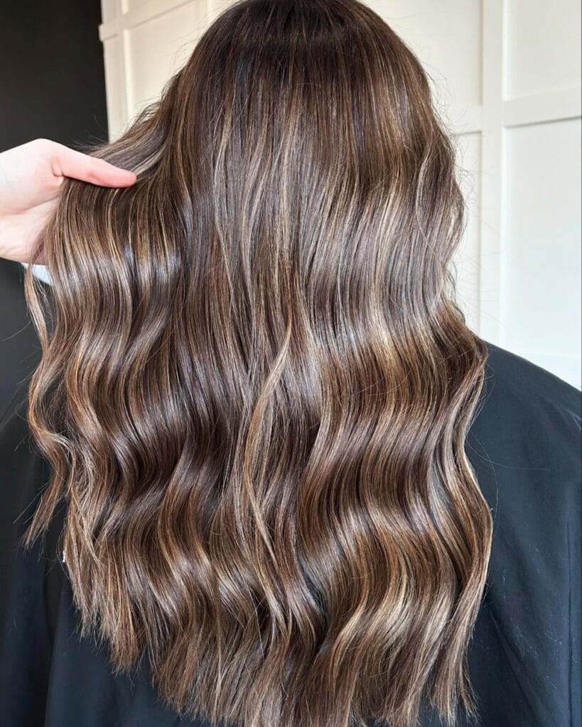 Long wavy brunette hair with soft sun kissed highlights and natural blend.