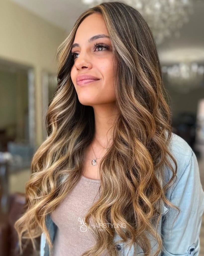 Long brunette hair with soft waves and blended caramel balayage highlights.