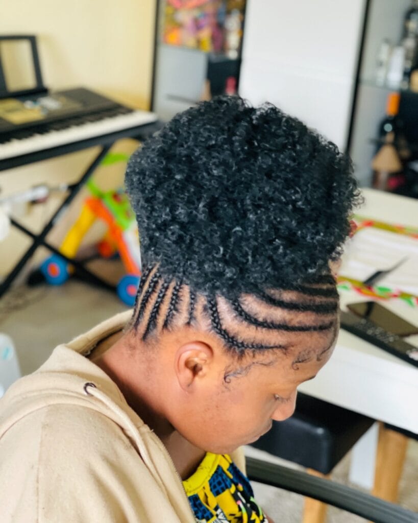 Cornrows braided upward into a high curly puff bun with defined natural texture.
