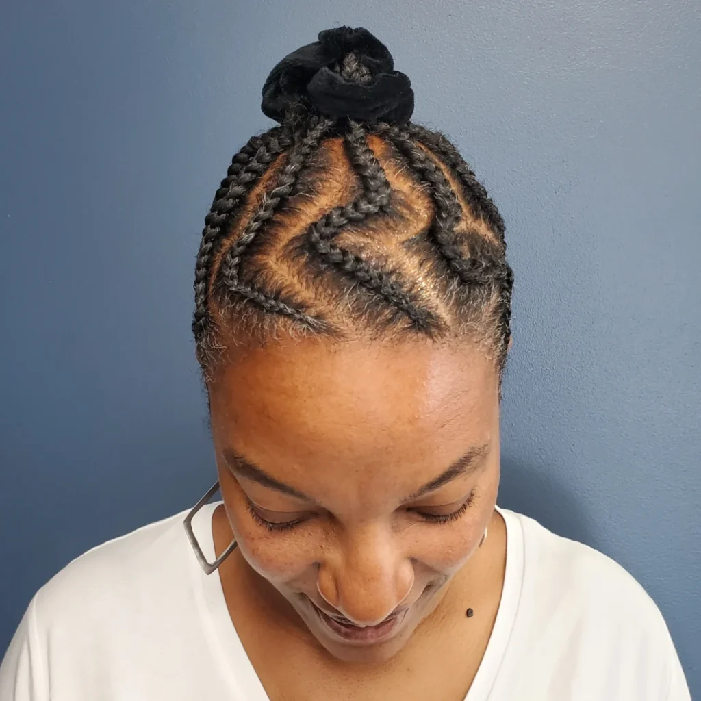 Zigzag patterned cornrows styled upward into a small braided bun.