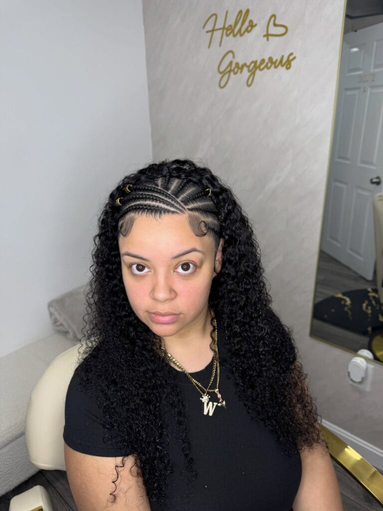 Front cornrows with gold hair rings flowing into long natural curly hair.