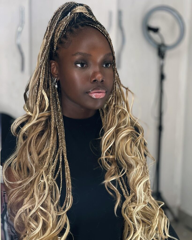 Honey blonde boho braids styled half up with long loose curls and dark roots.