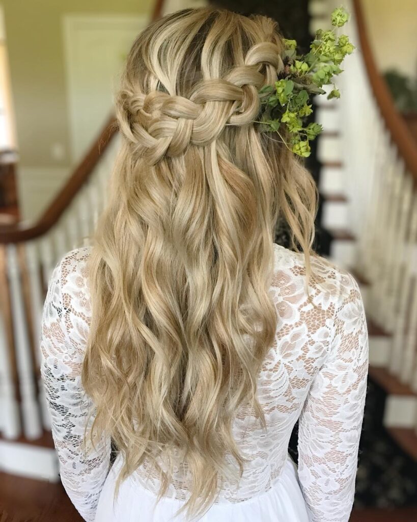 Blonde half up crown braid hairstyle with soft waves and small floral accents.