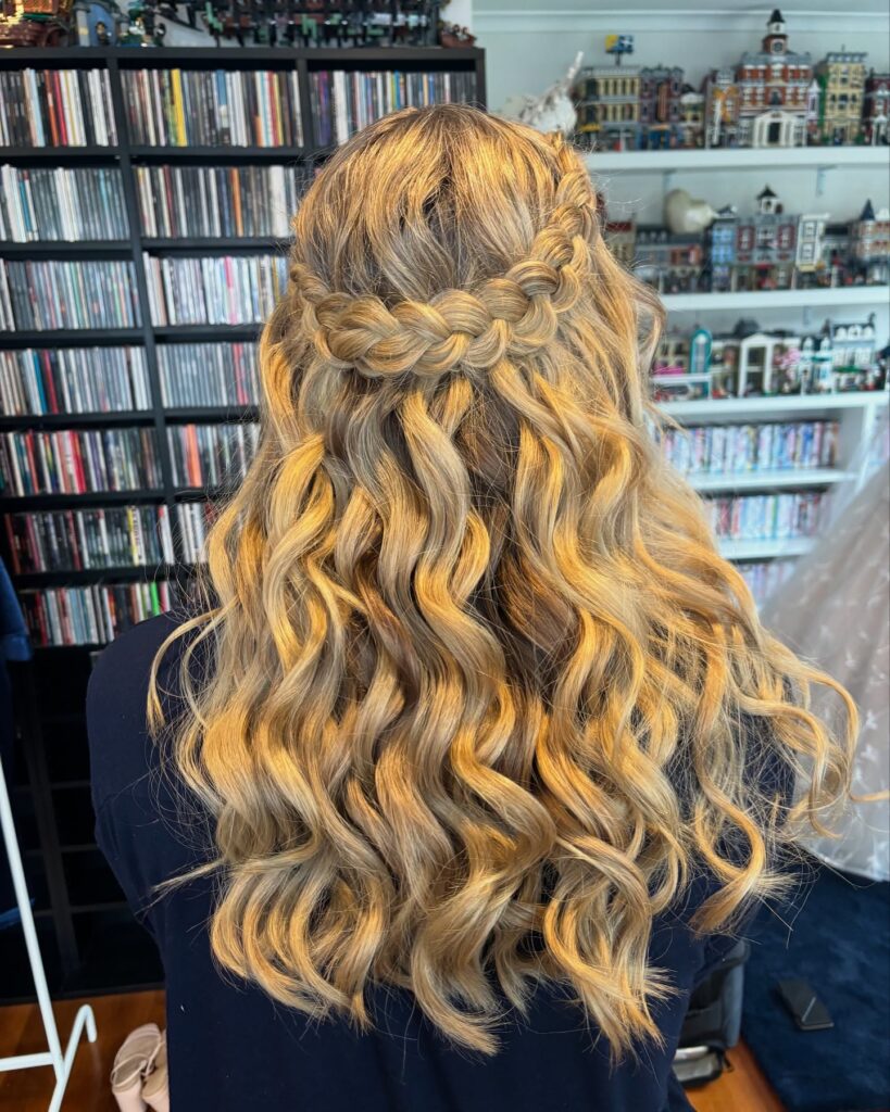 Long blonde wavy hairstyle with a loose braided crown across the back.