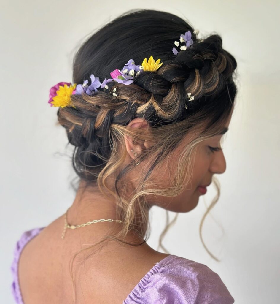 Chunky brunette crown braid hairstyle decorated with small colorful flowers.