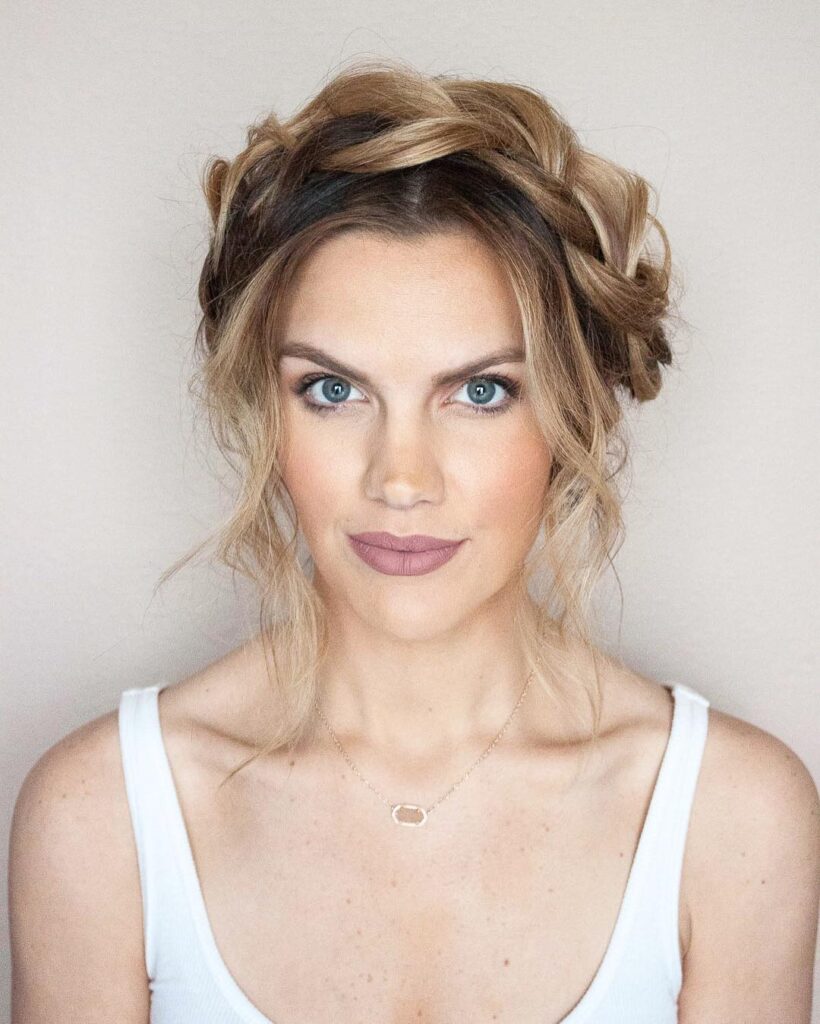 Loose braided crown bun hairstyle with soft blonde face framing pieces.