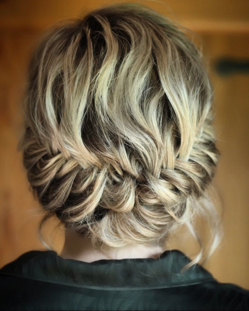 Blonde twisted crown hairstyle with a soft low bun and loose textured waves.