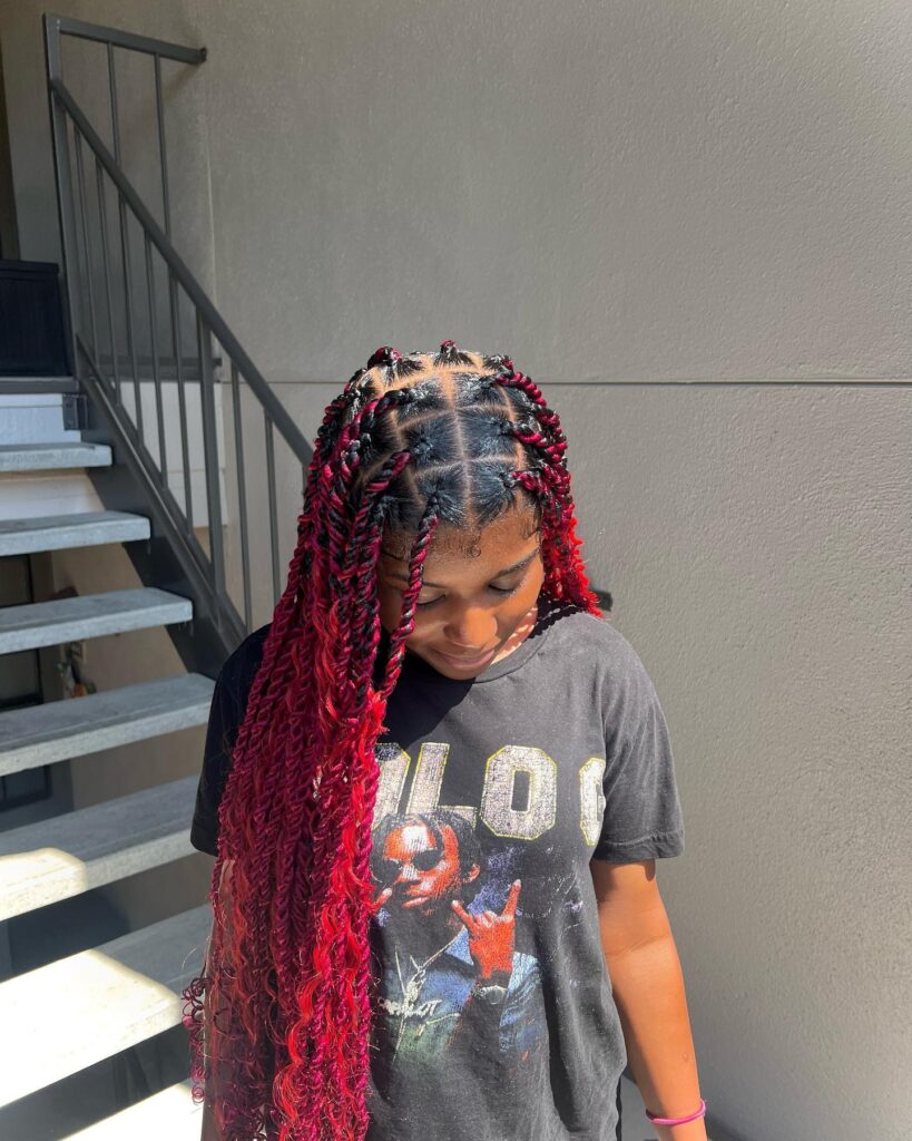 Island twist braids with black roots and bright red curly lengths.