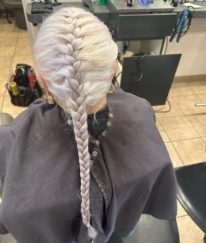 A long icy blonde French braid styled tightly down the back with a sleek finish.