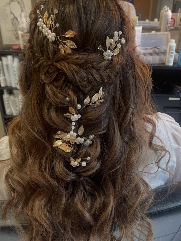 Long brunette wavy hair styled in a braided half up hairstyle with pearl leaf accessories.