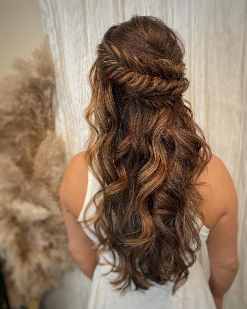 Long brunette hair with caramel highlights styled in loose waves and a twisted half up braid.