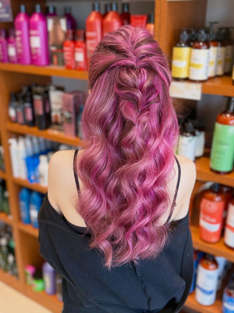 Long berry pink hair styled in loose waves with a half up pull through braid.